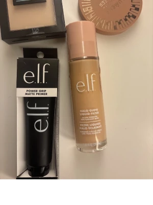 e.l.f. primer, foundation & bronzer - Säljer ett set med e.l.f. Power Grip Matte Primer i svart tub, Halo Glow Liquid Filter foundation med beige ton och ljusrosa lock, samt en rund bronzer i varm brun nyans. Perfekt för att skapa en jämn och glowig bas med snygg contour.