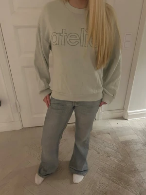 Beige sweatshirt från Atelier - Säljer en beige sweatshirt från Atelier med broderad logga framtill. Tröjan har en loose passform och långa ärmar, perfekt för en chill och avslappnad stil. Tillverkad i mjuk bomull som känns skön mot huden.