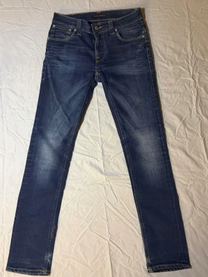 Nudie Jeans Mörkblå – Slim Fit – W28 L32 – Snygg tvätt med honeycombs - Säljer ett par Nudie Jeans i mörkblå färg, slim fit, storlek W28 L32, i mycket fint skick. Jeansen har en sjukt snygg tvätt med tydliga honeycombs som ger karaktär och premiumkänsla.  Klassiska Nudie-jeans med hög kvalitet och snygg passform. Perfekta för dig som gillar clean, stilren denim med detaljer.  • Märke: Nudie Jeans • Färg: Mörkblå • Storlek: W28 L32 • Passform: Slim fit • Skick: Mycket bra • Detaljer: Honeycombs • 100 % original  Nudie 1