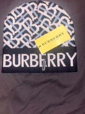 BB mössa - Snygg mössa från Burberry med ikoniskt monogrammönster i blått, vitt och svart. Stor logga framtill och vikbar kant. Tillverkad i mjukt stickat material som håller dig varm och stilsäker. Perfekt accessoar för dig som vill sticka ut.