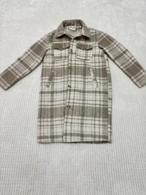 Rutig kappa från NA-KD i beige - Lång, rutig kappa från NA-KD i beige och vitt med klassisk krage, knappar framtill och två bröstfickor. Jackan har långa ärmar och är tillverkad i ett mjukt material med ullkänsla. Perfekt för lager-på-lager och chill stil.