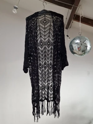 Black kimono - Black kimono, crochet/knit. Length: 120 cm (w/ fringe). Some loose threads, hence the price. It’s nothing I have noticed any of the times I picked it up, until now that I’m gonna sell it (not even when I picked it up from the secondhand store, obviously). It has been hanging untouched in my wardrobe for 3 years, because I just simply don’t reach for it. Now it’s time to move on :)