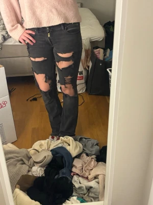 Svarta ripped lee jeans bootcut - Säljer ett par svarta lee jeans med slitna detaljer över låren och knäna. Modellen är bootcut med normal passning och klassisk femficksdesign. Jeansen har dragkedja och knapp framtill, och är tillverkade i jeansmaterial. 