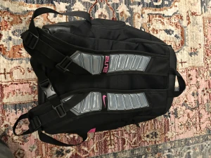 Svart Nike Elite ryggsäck med rosa detaljer - Nike Elite ryggsäck i svart med rosa logga och textdetalj. Snygg design med vadderade axelremmar och stora fack. Materialet är slitstark polyester och vissa delar har skinnliknande yta. Perfekt för dig som vill ha en sportig och praktisk väska med coola detaljer.