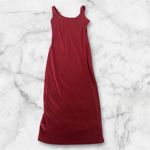 Rosa ribbad långklänning - Snygg rosa långklänning med ribbad struktur och smala axelband med slits i benet. Klänningen har en enkel, figurnära passform och ärmlös design som ger en clean och modern look. Perfekt för dig som gillar minimalistisk stil och vill sticka ut med färg.