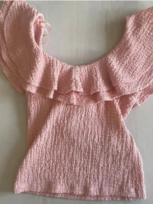 Rosa volang topp med offshoulder - Säljer en ljusrosa topp med offshoulder och bred volang runt axlarna. 