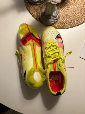 Nike Mercurial fotbollsskor gul/röd - Säljer ett par Nike Mercurial fotbollsskor i en riktigt fräsch gul färg med röda och svarta detaljer. Skorna har snörning, platt sula med dobbar och är tillverkade i lätt syntetmaterial med Flyknit-detaljer för extra komfort och passform. Perfekta för dig som vill sticka ut på planen. Storlek 44 och i princip oanvända!