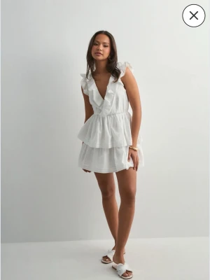 Vit studentklänning Nelly - Säljer en av studentklänningarna som jag valde att inte ha, då jag fick hem den i en storlek för stor. Det är en supersöt vit kortklänning från Nelly med omlott och volangdetaljer. Klänningen har v-ringning, öppen rygg med knyt och dubbla lager i kjolen. Passar perfekt till student eller skolavslutning💗