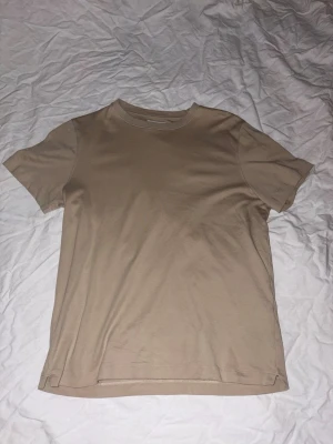 Beige t-shirt från These Glory Days - Snygg beige t-shirt från These Glory Days i storlek small. Modellen är klassisk med rund hals och korta ärmar, tillverkad i mjuk bomull. Perfekt för dig som gillar stilrena och enkla plagg med en neutral färgton.