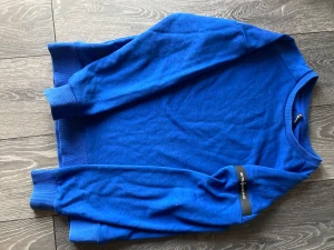 Blå Sail Racing sweatshirt i bomull - Snygg blå sweatshirt från Sail Racing i storlek M. Tröjan har rund hals, ribbade muddar vid ärmslut och nederkant samt diskret logga på ärmen. Perfekt för dig som gillar stilrena och sportiga plagg. Materialet är mjuk bomull som känns skönt mot huden.