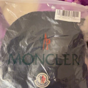 Svart ribbad mössa från Moncler - Snygg svart ribbad mössa från Moncler med broderad logotyp framtill. Perfekt för att hålla värmen med stil. Mössan är tillverkad i ett mjukt och bekvämt material.