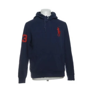 Marinblå hoodie från Polo Ralph Lauren - Snygg marinblå hoodie från Polo Ralph Lauren med röd logga på bröstet och en stor röd siffra 3 på ärmen. Tröjan har huva med snörning, känguruficka och långa ärmar. Perfekt för dig som vill ha något trendigt 
