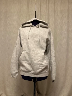 Grå hoodie från Jack & Jones - Snygg ljusgrå hoodie från Jack & Jones med klassisk känguruficka och snörning vid huvan. Mjuk insida i fleece och normal passform. Perfekt för chill dagar och enkel att matcha med jeans eller joggers.