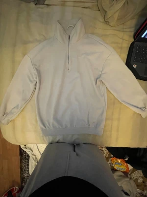 Ljusgrå fleece-tröja med half zip - En stilren ljusgrå fleece-tröja med hög krage och half zip framtill. Tröjan har långärmade ärmar och ribbade muddar vid midja och ärmslut. Perfekt för kyliga dagar och enkel att matcha med jeans eller mjukisbyxor.