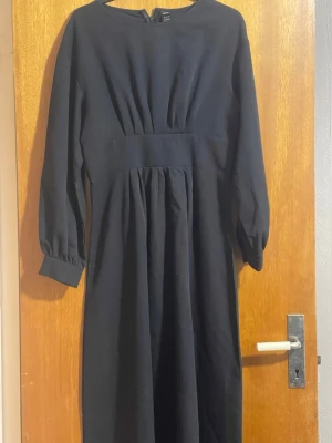 Svart långärmad långklänning - En stilren svart långklänning med långa ärmar och markerad midja. Klänningen har rund halsringning och lätt puffade ärmslut för en elegant look. Perfekt för dig som gillar minimalistisk och klassisk stil. Den kommer inte med ett bälte. ❤️❤️