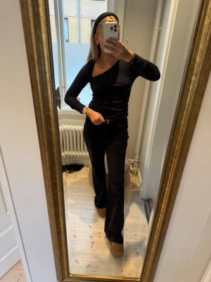 Svart topp med lång ärm - Säljer en svart, slim oneshoulder topp med lång ärm. Toppen har en cool asymmetrisk skärning över axeln och sitter tight mot kroppen. Perfekt för dig som gillar minimalistisk stil med en twist. Materialet känns mjukt och stretchigt, troligen polyester eller bomull.