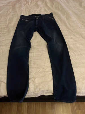 Replay Grover straight fit jeans blå - Snygga mörkblå Replay Grover jeans i straight fit med klassisk femficksdesign och diskreta slitningar. Byxorna har normal passform och är tillverkade i stretchigt jeansmaterial för extra komfort. Perfekta för dig som gillar stilrena och tidlösa jeans.