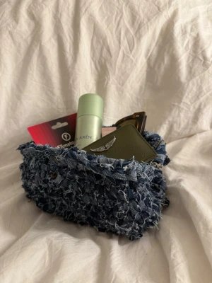 Blå handväska i denim med fransar - #015 - blå. En unik handväska i blå denim med cool fransad yta. Väskan har en mjuk, rundad form och är perfekt för att bära småsaker. Materialet är denim och ger en trendig vibe. Perfekt för dig som gillar statement-accessoarer och vill sticka ut.