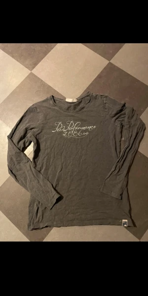 Mörkgrå långärmad Peak Performance tröja - Säljer en mörkgrå långärmad tröja från Peak Performance med vit textprint på bröstet. Superskön men kommer ej till användning