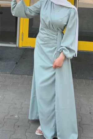 Ljusgrön långklänning med omlott - Superfin ljusgrön långklänning med omlott-detalj i midjan och ballongärmar. Klänningen har en elegant, flowy passform och är tillverkad i ett mjukt, slätt material. Perfekt för dig som gillar stilrena och trendiga looks.