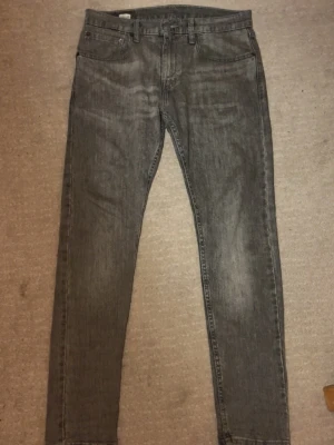 Levi's grå jeans W31 L32 skinny - Snygga grå jeans från Levi's med skinny passform och klassisk femficksdesign. Jeansen har en mörkgrå tvätt och är tillverkade i slitstarkt bomullsmaterial. Perfekt för dig som gillar en smal siluett och vill ha ett stilrent plagg i garderoben.