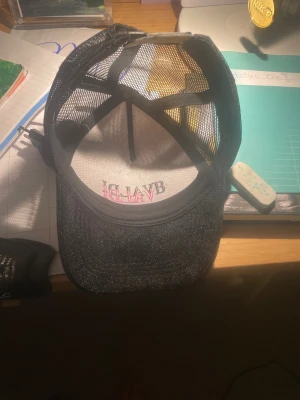 BVALDI svart och vit truckerkeps - Snygg truckerkeps från BVALDI med svart glittrig skärm och vit frontpanel ny pris 499.  Kepsen har broderad logga i svart och rosa, samt mesh på sidorna och bak för extra ventilation. Perfekt för att lyfta din streetstyle-look och bli mer populär 