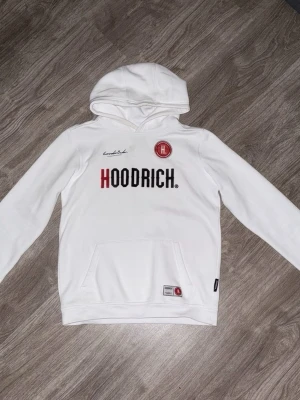 Hoodrich Hoodie - Vit Hoodrich hoodie med huva och magficka. Hoodrich märket finns på både fram och baksidan. Hoodien har samt en bekväm passform.