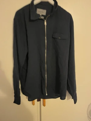 Mörkblå overshirt från Elvine - Snygg mörkblå overshirt från Elvine med hel dragkedja framtill och en bröstficka med knapp. Tillverkad i bomull och har en klassisk krage. Perfekt för lager-på-lager och chill stil.