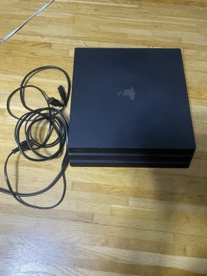 PlayStation 4 Pro - Sony PlayStation 4 Pro spelkonsol i svart, med tillhörande strömkabel och HDMI-kabel. Konsolen visar mindre yttre slitage och damm, men är i gott skick. Perfekt för dig som vill spela de senaste spelen med hög prestanda och 4K-stöd.