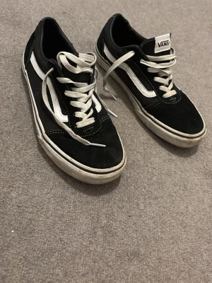 Svarta Vans Old Skool sneakers - Svarta Vans Old Skool sneakers med vit sidorand och vita snören. Klassisk låg modell med rund tå och platt sula i gummi. Ovandel i mocka och canvas, insida i textil. Perfekta för dig som gillar streetstyle och skate.