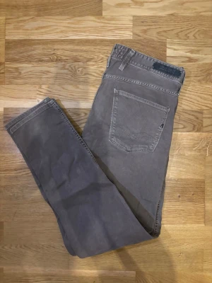 Replay Anbass - Säljer ett par gråa Replay jeans i slim passform, storlek 34/32. Byxorna har klassisk femficksdesign, normal midja och raka ben. Materialet är mjuk bomull med lite stretch för extra komfort. Snygga detaljer med Replay-logga på bakfickan och läderpatch vid linningen.