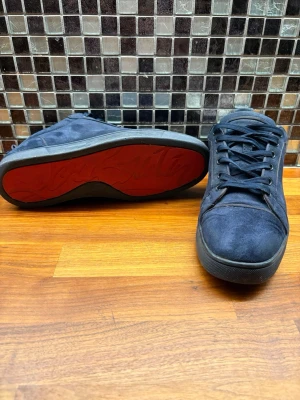 Mörkblå sneakers från Christian Louboutin - Säljer ett par mörkblå sneakers från Christian Louboutin med klassisk röd sula och broderad logga på hälen. Skorna är gjorda i mocka. Lågt pris pågrund av skada på mockan se sista bilden samt att mockan på vänster sko har släppt på ena sidan pågrund av vatten skada. (Ingen box) endast Christian Louboutin kortet, bild kan skickas.  BVSA!!!