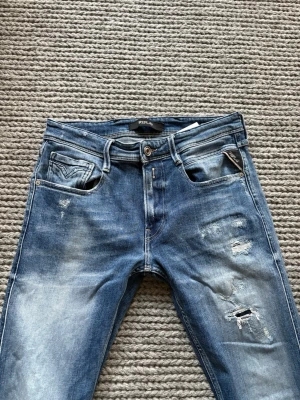 Replay anbass - Replay Anbass w 31 L 32 Längd 100 cm midjemått 37x2 cm! Jeansen har snygga slitningar med en fräsch fade och i mycket fint skick förutom att läderlappen bak på byxan är avryckt tyvärr men det tänker man inte på! Sitter slim.