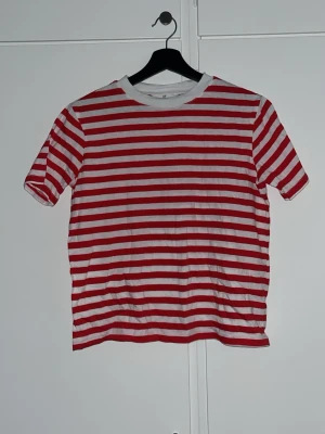 Randig röd och vit t-shirt - Säljer en klassisk t-shirt från H&M med röda och vita horisontella ränder. T-shirten har rund hals och korta ärmar, perfekt för dig som gillar en enkel men ändå färgstark stil. Materialet är mjuk bomull och är från H&M. Använd 1 gång till Kent konserten för lite Hagnesta Hill vibe