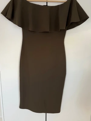 Brun offshoulder klänning  - Snygg brun klänning från PNK i offshoulder-modell med bred volang. Klänningen passar fester, bröllop eller nyårsklänning. Den har inga defekter då den är använd endast en gång. 