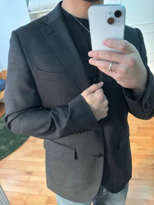 Mörkgrå kavaj från Riley Slim Fit - Säljer en gammal kavaj jag aldrig använt som jag fick som gåva för 4 år sen.        Tyvärr finns inte någon utsatt storlek men jag är 170 så man bör inte vara längre än så om man vill att den ska passa bra som slim fit