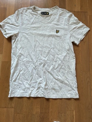 Vit prickig t-shirt från Lyle & Scott - Säljer en vit t-shirt från Lyle & Scott i storlek M. T-shirten har korta ärmar och är dekorerad med små färgglada prickar samt en broderad gul logga på bröstet. Materialet är mjuk bomull och passformen är normal. Perfekt för dig som gillar stilrena detaljer.