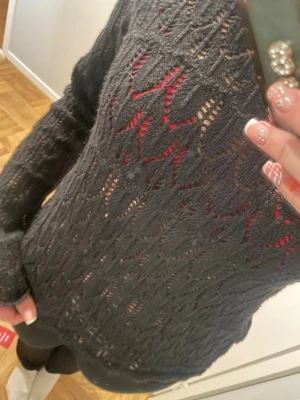 Svart stickad tröja från Vero Moda - Säljer en svart stickad tröja från Vero Moda med snyggt hålmönster. Tröjan har lång ärm och är lite genomskinlig vilket gör den extra cool att styla med färgglada toppar under. Perfekt för dig som gillar en unik och trendig look. Ganska liten i storlek.