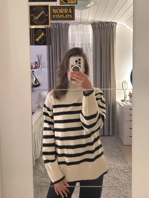 Randig polotröja i svart och beige - Säljer en mysig polotröja med svarta och beige ränder. Tröjan har hög krage, långa ärmar och breda ribbade muddar. Oversized fit som är perfekt för lager-på-lager. Stickad i mjukt material och passar perfekt till jeans eller leggings. Använt 1-2 gånger och tycker att den sitter mjukt på huden och inte stiks. säljer pga jag inte gillar hög krage!🤍🤍