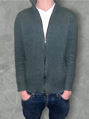 Massimo Dutti cashmere Full zipStorlek S - Massimo Dutti Cashmere Full-Zip – Grågrön – Strl S Exklusiv full-zip-tröja i en mjuk och lyxig cashmere-mix. Modellen har en stilren tvåvägsdragkedja, hög krage och en perfekt passform som både känns och ser premium ut. Färgen är en snygg grågrön ton som funkar till allt. Tröjan är i riktigt bra skick, utan noppor eller slitage. Kostar ca 3000 kr ny pris! Ett riktigt kap. ✓Cashmere-mix – supermjuk & varm ✓Tvåvägsdragkedja ✓Slim/regular passform ✓Snygg grågrön färg