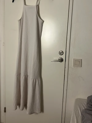 Vit långklänning - Pris går att diskutera/ tvätt ingår innan leverans 💗 Säljer en vit långklänning i storlek XS. Klänningen har smala axelband, rak halsringning och ett snyggt rynkat parti nedtill som ger extra volym. Materialet är mjukt och har en lätt struktur som känns skönt mot huden. Perfekt för varma dagar.  