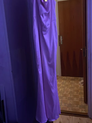 Balklänning Lila långklänning från Marthea - Säljer en snygg balklänning  lila  långklänning från Marthea med smala axelband och mjukt, glansigt tyg. Klänningen har en elegant draperad halsringning och är figurnära i modellen. Perfekt för dig som vill sticka ut med en färgstark look.