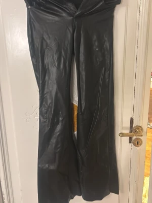 Svarta bootcut byxor i skinnimitation - Säljer ett par svarta bootcut-byxor i skinnimitation mid wais. Tyvärr sönder jylf