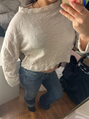 Ljusbeige croppad stickad tröja - Säljer en ljusbeige croppad stickad tröja med lång ärm och ribbad kant vid hals och ärmslut. Tröjan är mycket nopprig och skrynklig