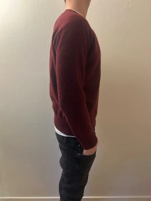 Vinröd stickad tröja från Oscar Jacobsson  - Snygg vinröd stickad tröja med rund hals och långa ärmar. Tröjan har en enkel och klassisk design som passar perfekt till jeans. Materialet är mjukt och ger en skön känsla, perfekt för kyliga dagar. Bara att höra av er vid funderingar!