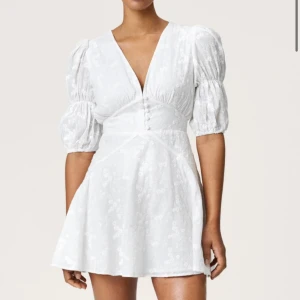 Studentklänning!! - Superfin vit kort klänning med v-ringning, puffiga korta ärmar och knappar framtill. Klänningen har ett subtilt blommigt mönster och markerad midja som ger en snygg siluett. Perfekt för sommarens alla tillfällen!