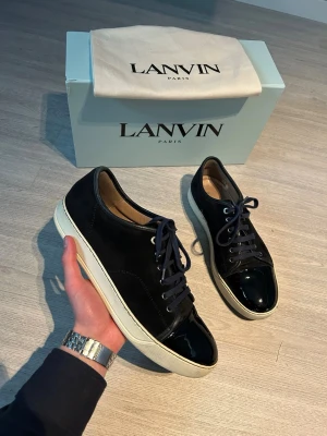 Lanvin (stl 43) - Lanvin sneakers i marinblå mocka med snygg lackad tå och vit platt sula. Skorna har snörning och en stilren, rund form. Perfekt för dig som gillar exklusiva och trendiga sneakers med en unik touch. Kommer med originalkartong och dustbag från Lanvin Paris.