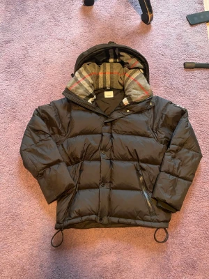 Burberry jacka / väst, M/S - Burberry jacka i storlek M (men sitter bra som storlek S), svart färg och tillverkad av dun.   Varm och bekväm Burberry-jacka i stilren design. Jackan har avtagbara ärmar och kan enkelt användas som väst, vilket gör den flexibel för olika väder. Skön passform med huva – perfekt för både vardag och utomhusbruk.