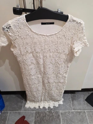 Vit spetsklänning från Oui - Supersöt vit kortklänning från Oui med blommigt spetsmönster och rund hals. Klänningen har korta ärmar och fina spetsdetaljer längst ner. Materialet är en mix av bomull, viskos och elastan vilket gör den mjuk och bekväm. Perfekt för sommarens alla tillfällen!
