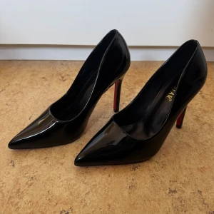 Svarta klackskor - Svarta klackskor med glansig lackyta och röd sula. Skorna har spetsig tå och hög klack. 